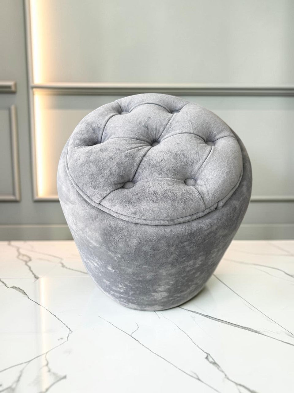 Banco Leisecester de CASA GARRIDO Muebles, taburete redondo gris capitoneado con almacenamiento y tapizado suave.