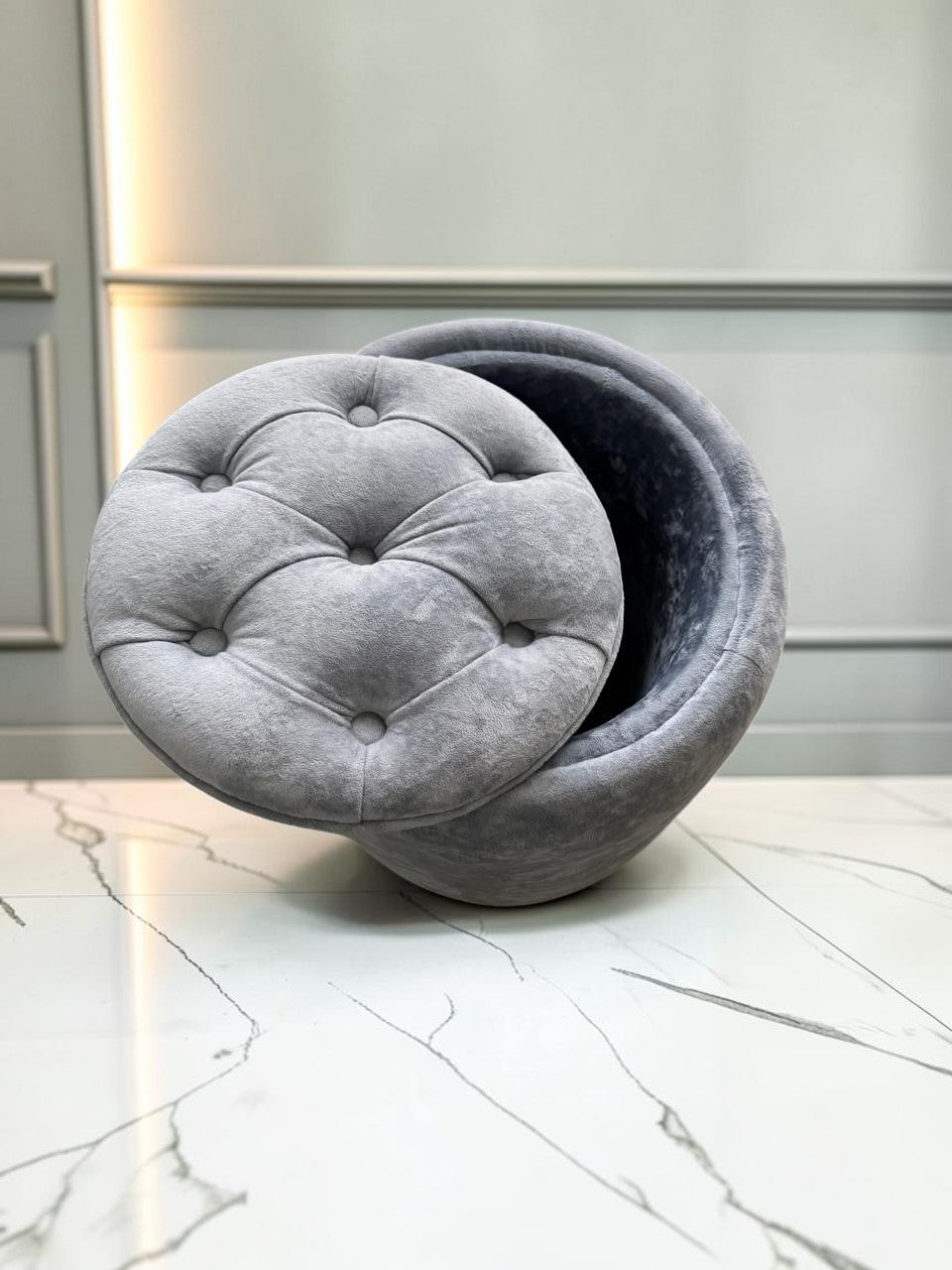 Banco Leisecester de CASA GARRIDO Muebles, baúl redondo gris capitoneado con almacenamiento interno y tapizado suave.