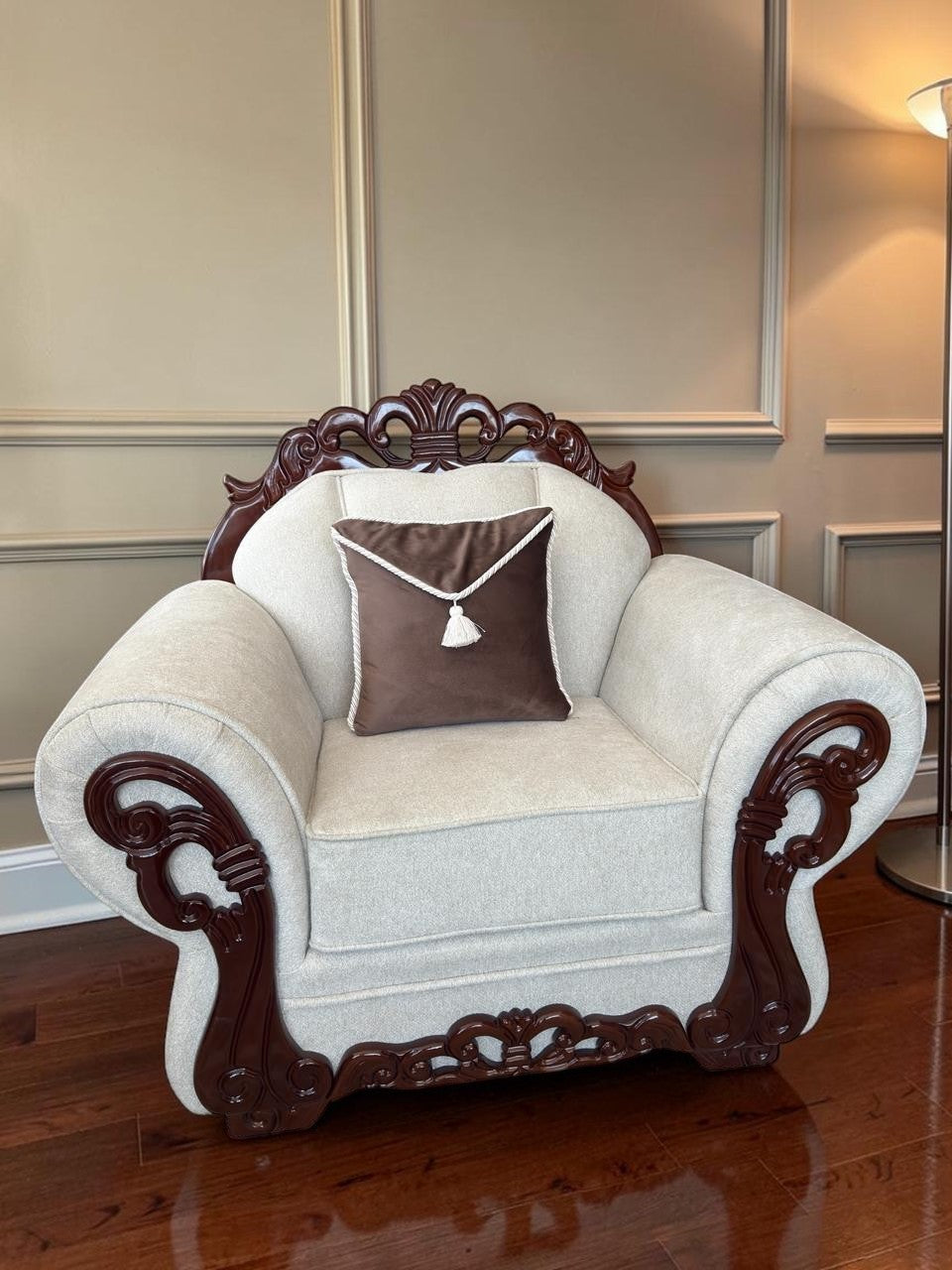 Sillón Carey de CASA GARRIDO Muebles con tapizado beige, estructura de madera tallada oscura y cojín marrón decorativo
